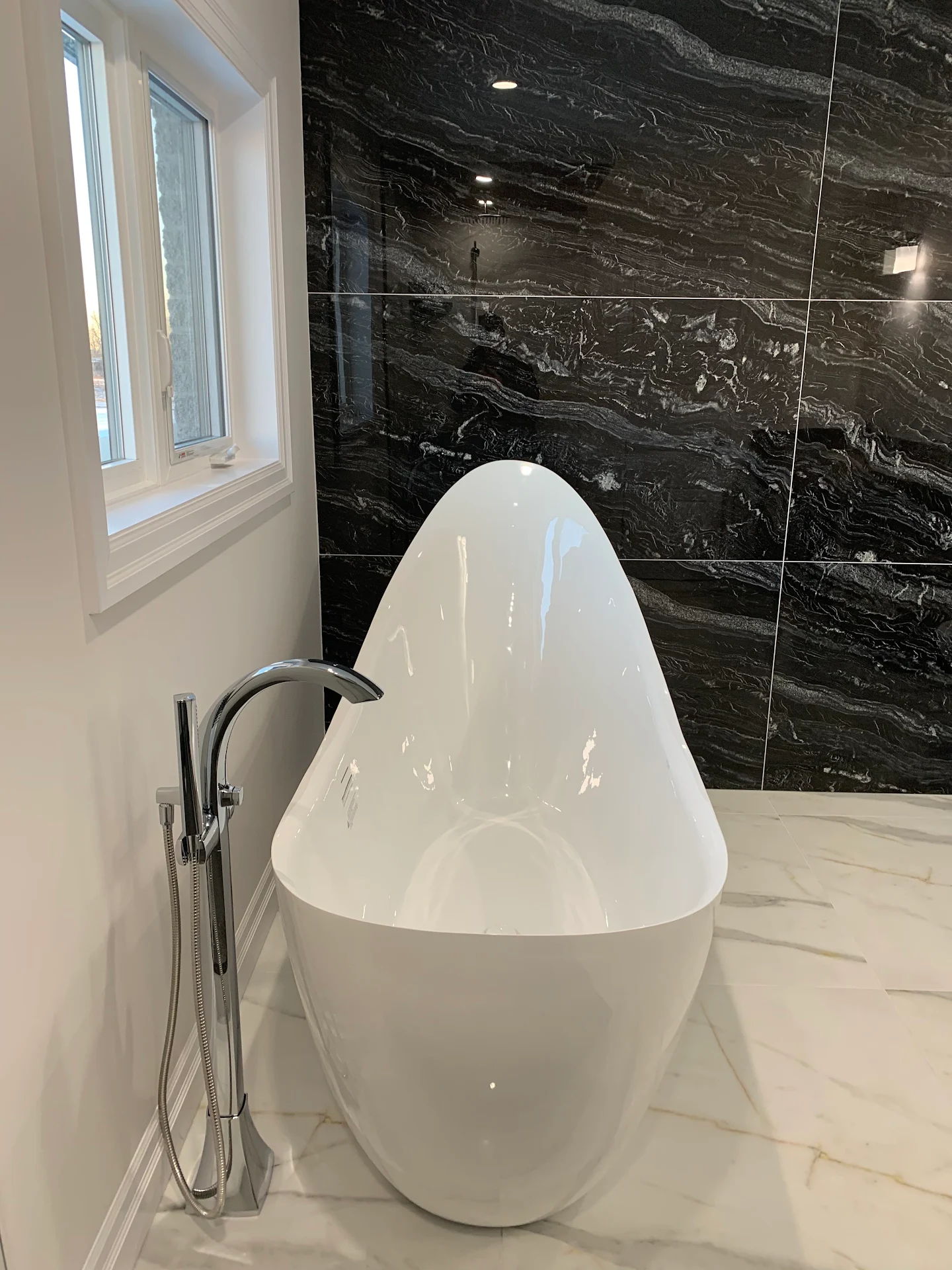 Apex Plumbing freestanding bathtub installation with a chrome floor-mounted faucet against dark marble tile